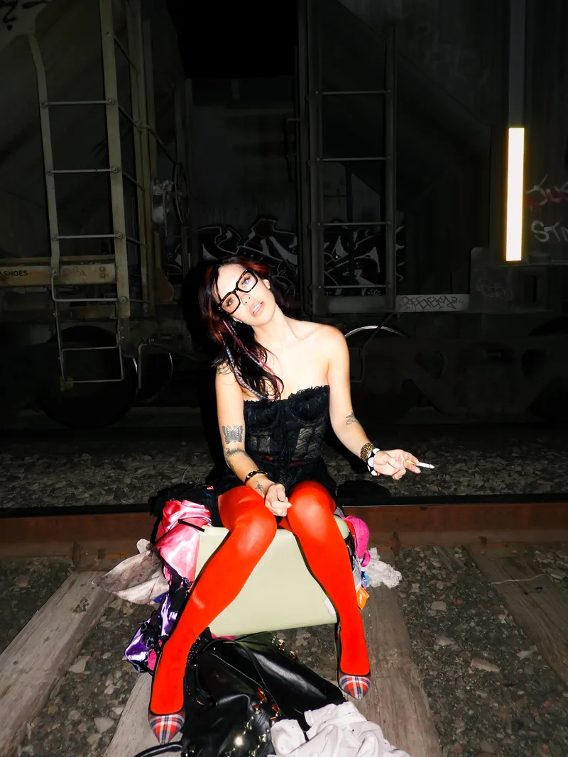Woman in glasses and red tights sitting on train tracks at night, flash-lit