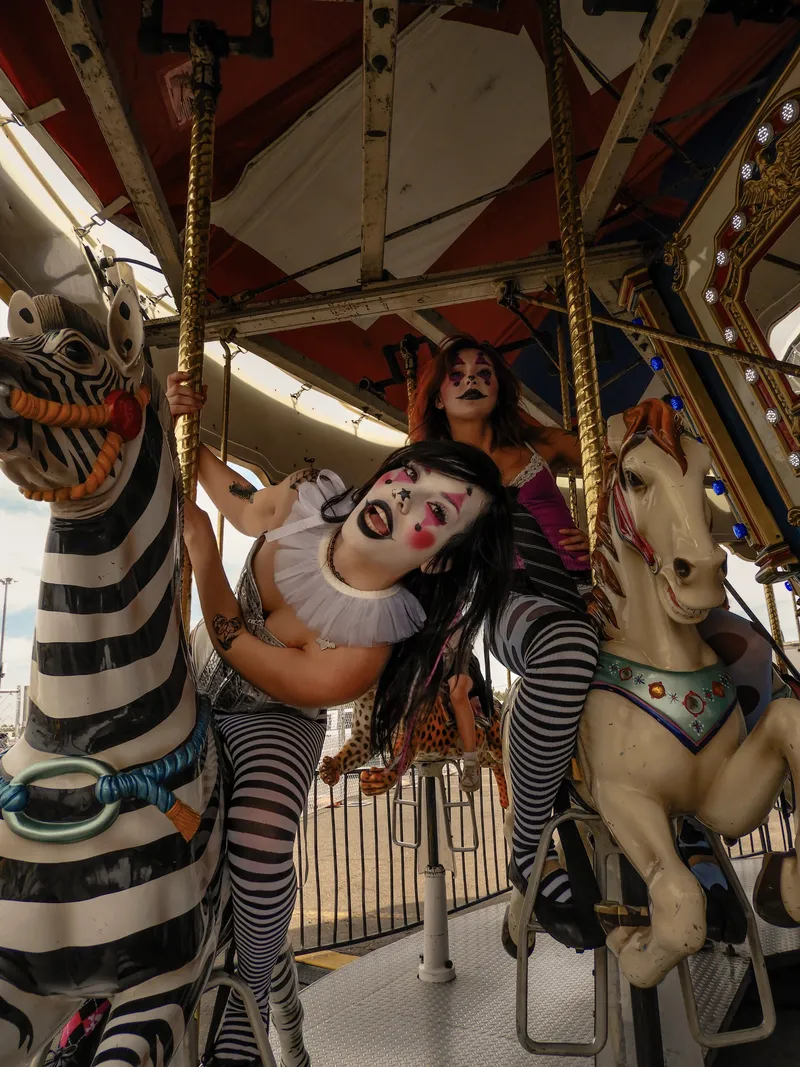 Two women in clown makeup riding a carnival carousel