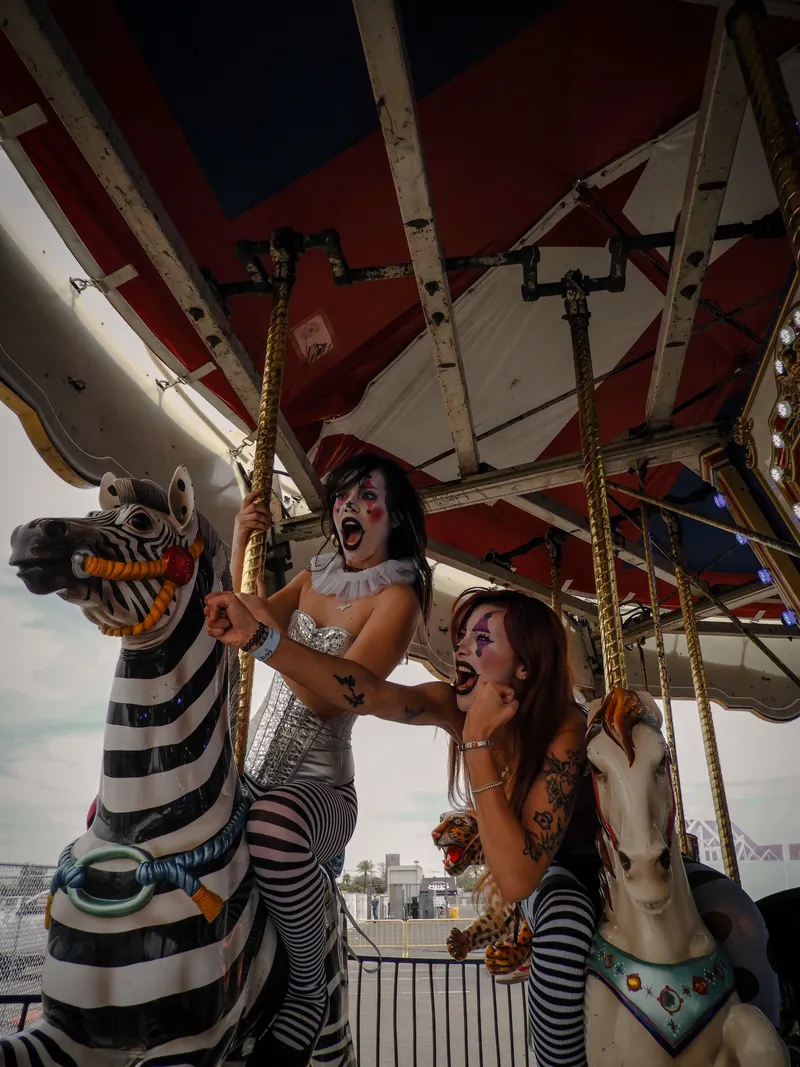 Two women in clown makeup shouting on carousel animals