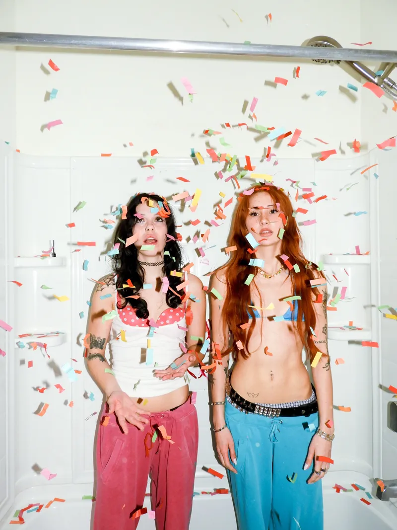Two women standing in a bathtub as confetti falls around them